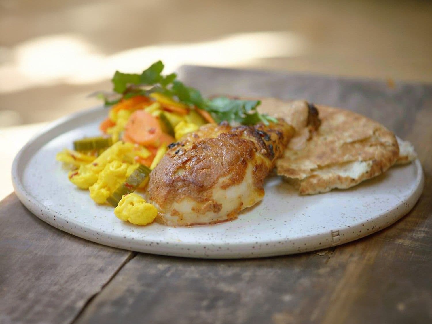 Kip tandoori aan het spit met opgelegde groenten en naan